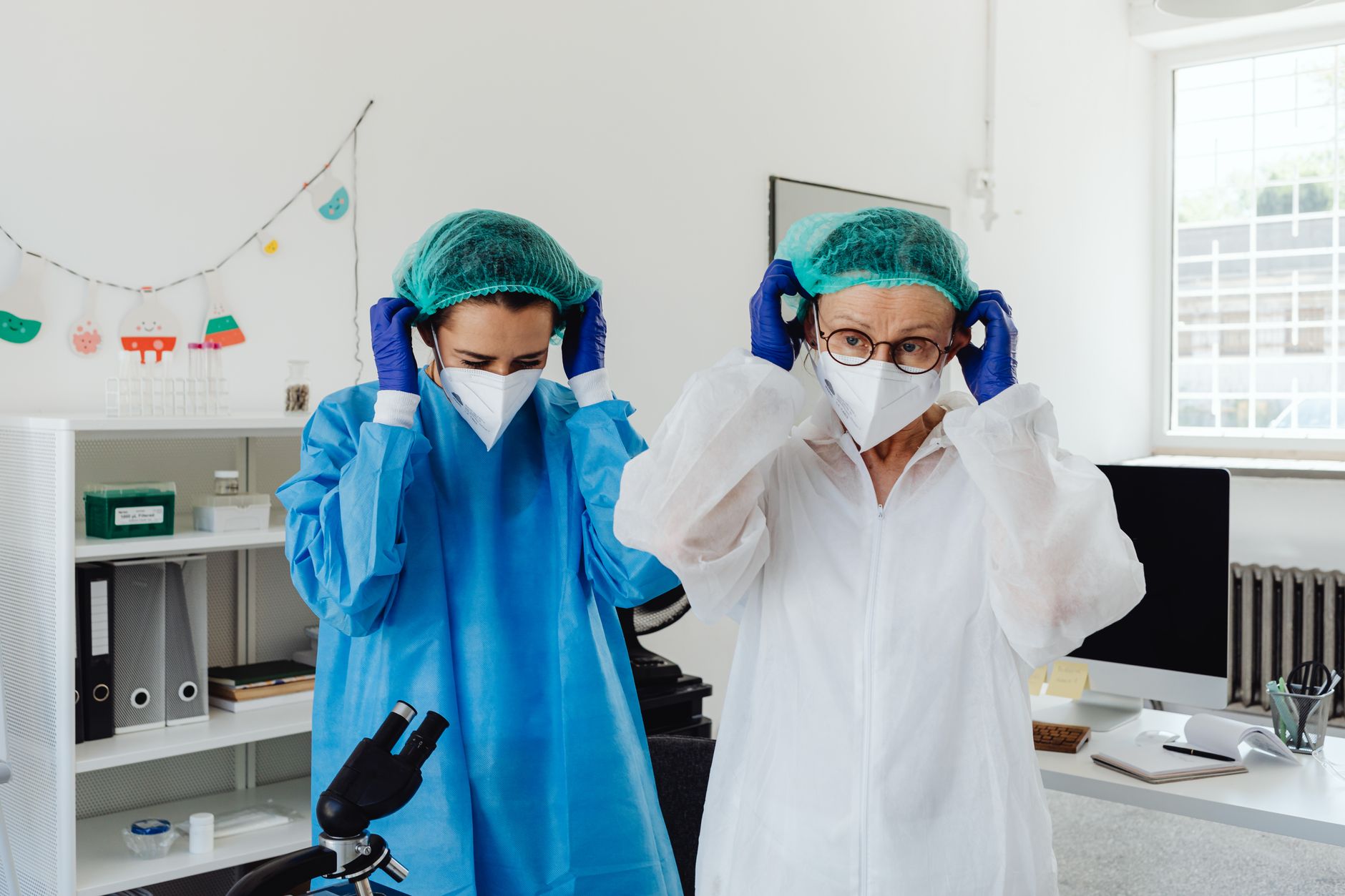 Two healthcare workers putting on protective gowns, caps and masks