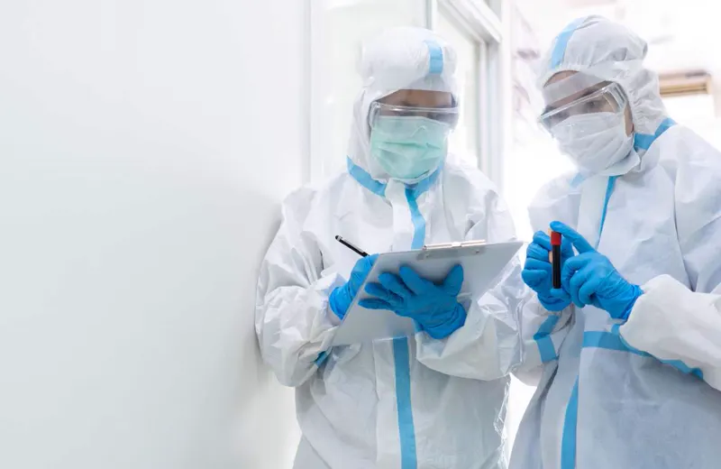 Two healthcare workers in full protective suits reviewing a clipboard