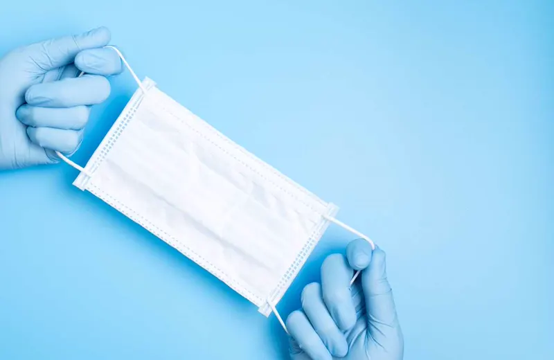 Gloved hands holding a disposable surgical face mask